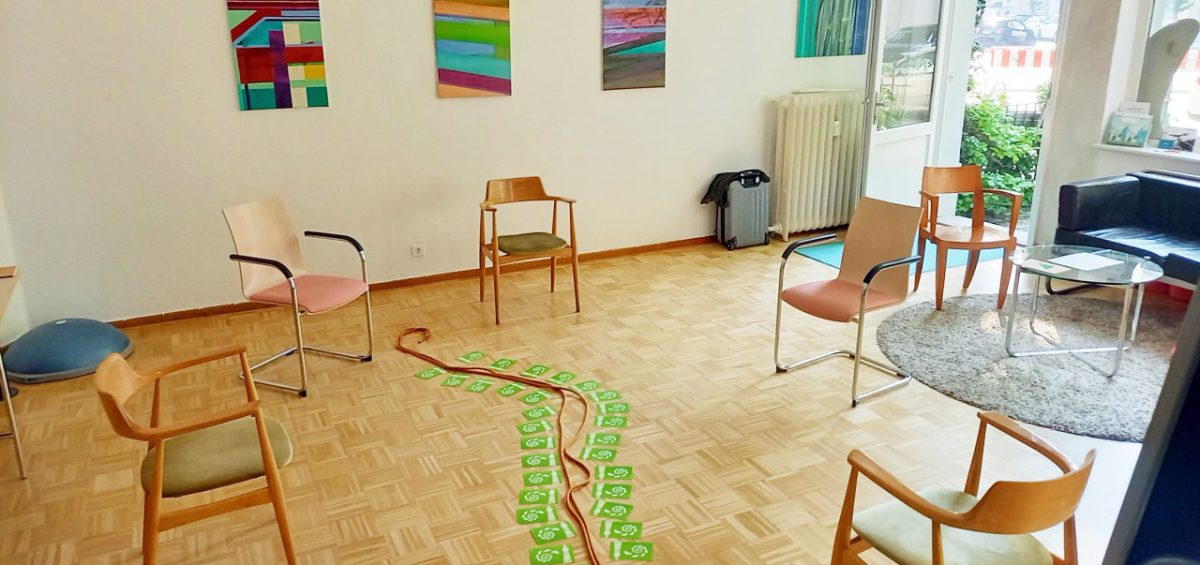 Raum mit Stuhlkreis, in der Mitte liegt ein Seil umrahmt mit grünen Kärtchen.